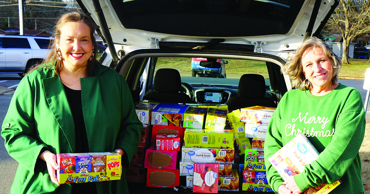 Two women posing with food donations collected in the back of a SUV