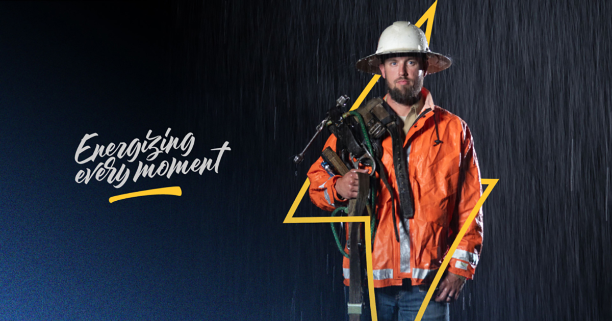 lineworker wearing high-visibility jacket and hard hat, holding equipment needed to climb light pole with the slogan Energizing Every Moment to his left