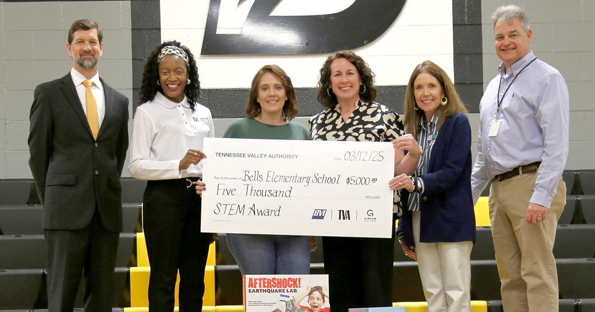 Photograph showing a group of six adults standing next to each other. The four women in the middle are holding an oversized grant check.