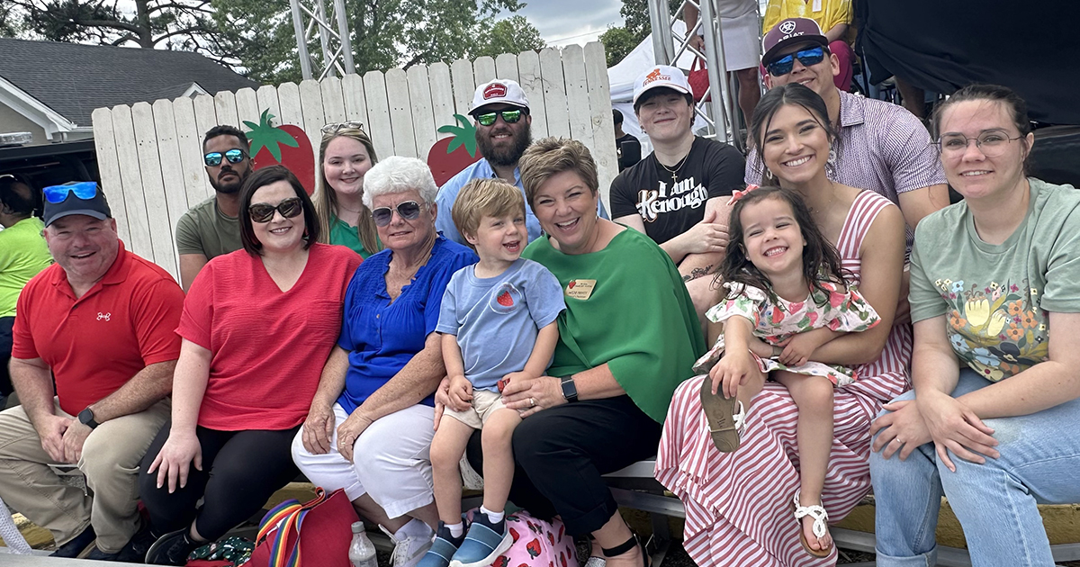 Photo showing a family sitting together on stadium bleachers at the West Tennessee Strawberry Festival. There are adults and children in the photo, and everyone is smiling.