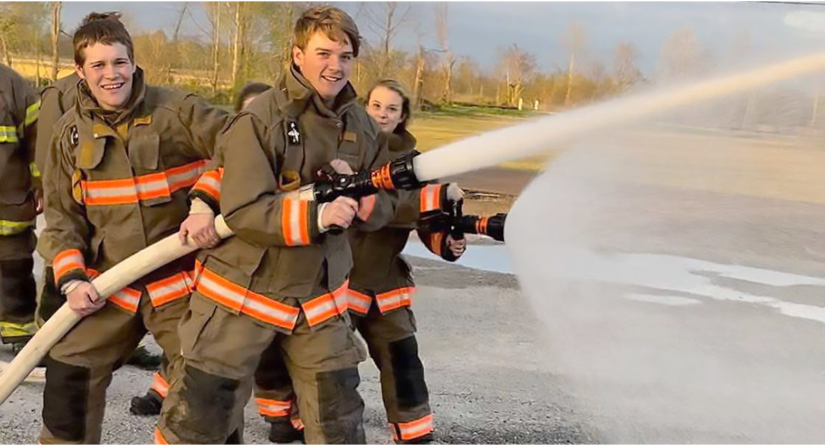 Photo of high school students spraying water from a fire hose for a training exercise
