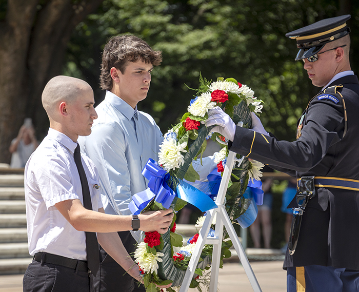Two male students wearing dress pants, dress shirts and neckties present a colorful wreath to a soldier in dress uniform at the Tomb of the Unknown Soldier in Washington, D.C.