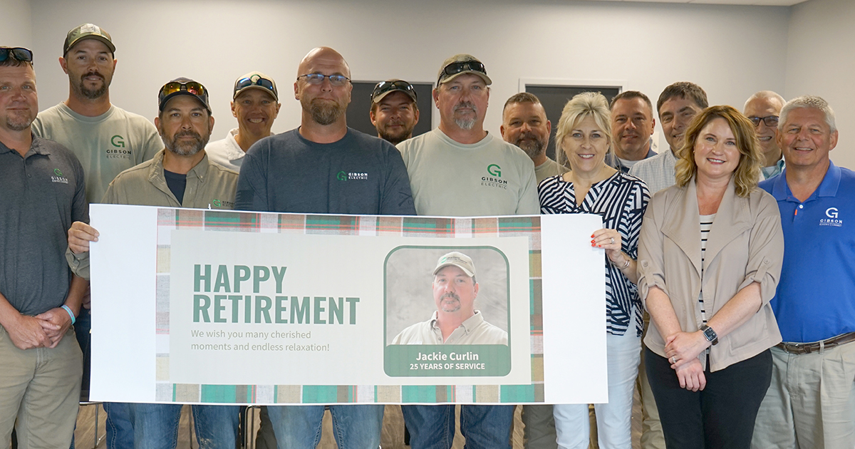 Several men and women stand, holding a sign that reads, "Happy Retirement" for Jackie Curlin