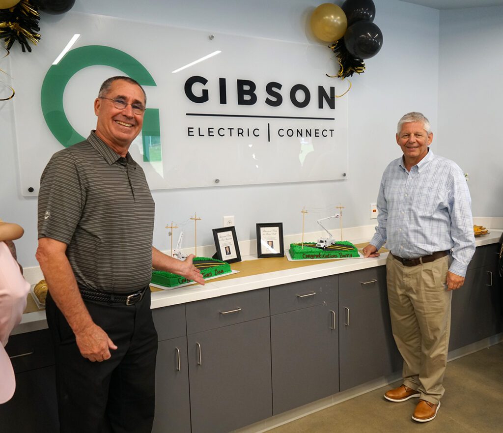 Dan Rodamaker and Barry Smith pose with their cakes at their retirement reception. Each cake features a miniature bucket truck, poles and power lines.