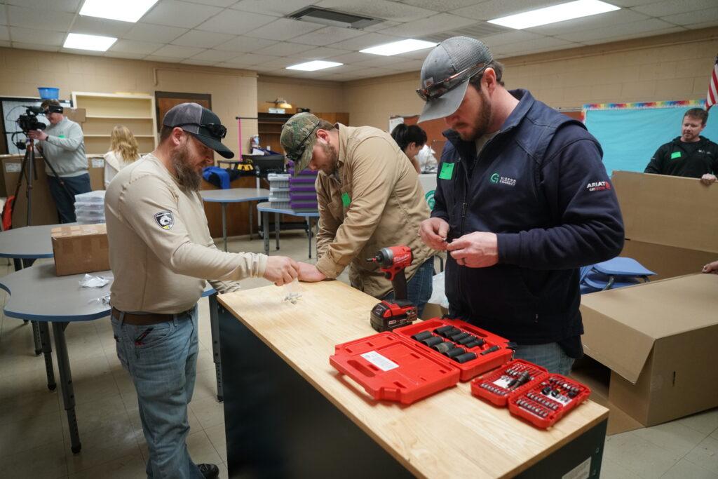 Three Gibson Electric team members assemble furniture for the Ripken Foundation STEM Center inside a classroom at Margaret Newton Elementary School, using hand tools and a cordless drill.